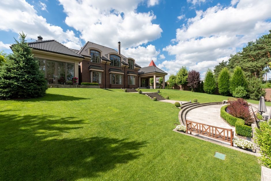 Elegant brick mansion with manicured lawn and garden under a bright blue sky.